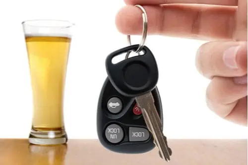 Hand holding car keys next to a glass of beer
